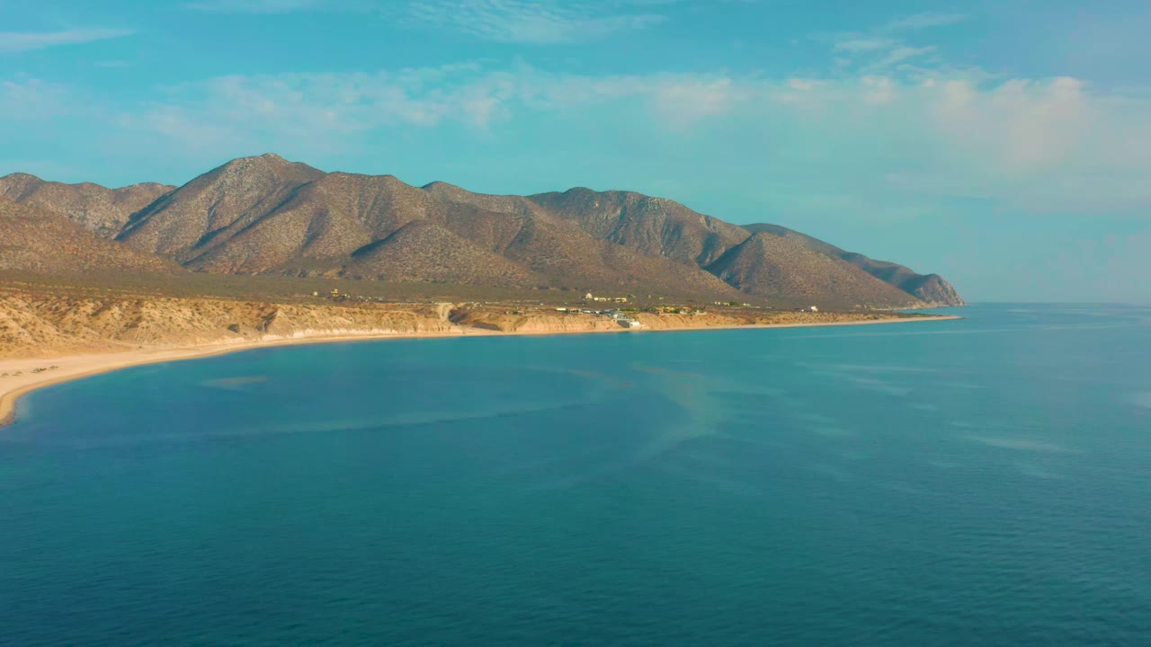 Aerial coastline with calm blue sea and low brown mountains.
