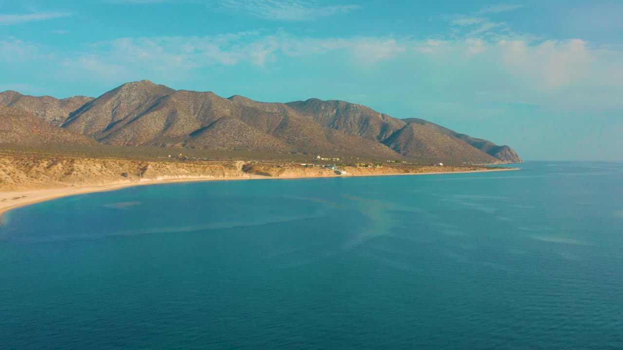 Frame at two seconds shows the blue water foreground, a curving sandy beach on the left, rugged brown hills behind the shore, and no visible people.