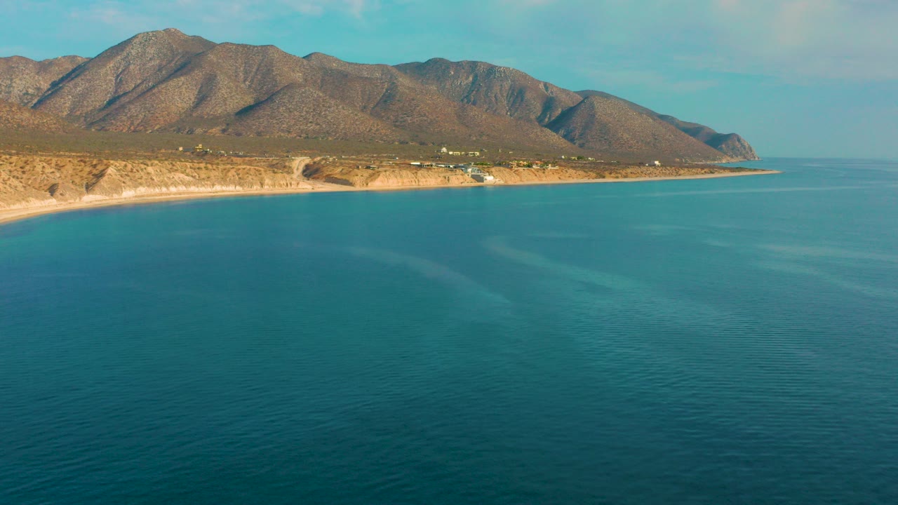 Opening frame of El Sargento La Ventana, Mexico, with blue ocean in the foreground, a tan shoreline and brown mountain range beyond it, and no visible people.