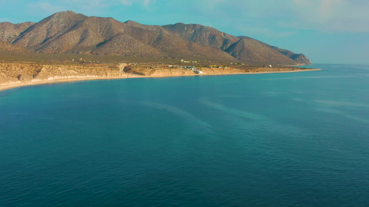 Frame at 0:02 shows the El Sargento La Ventana shore running horizontally across the image, with blue sea below, a brown mountain ridge above, and no visible people.