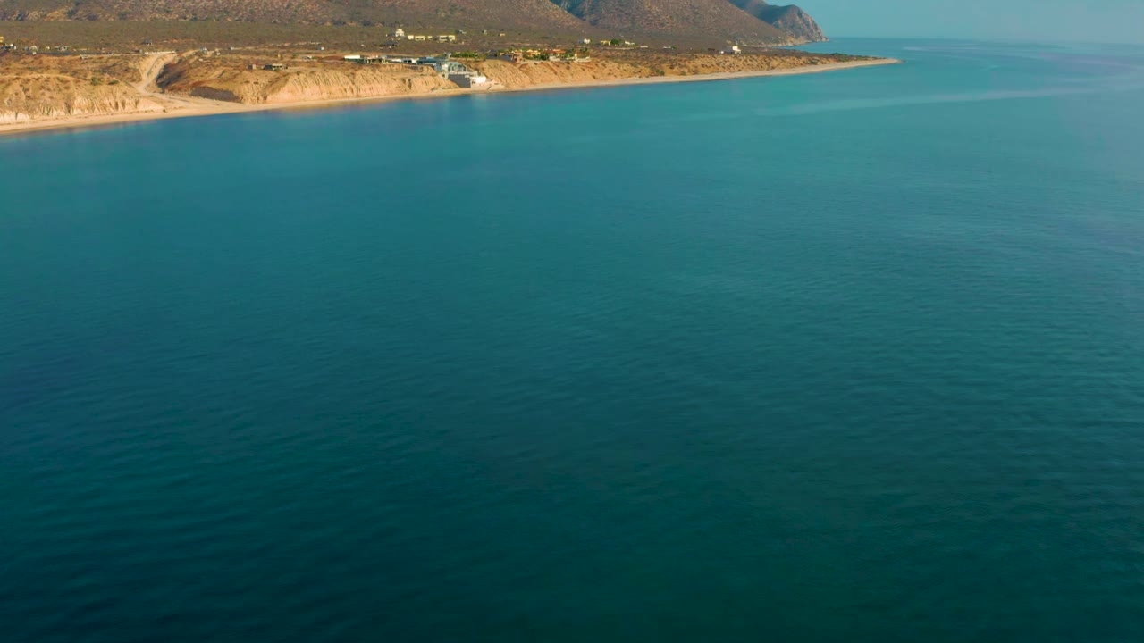 Aerial view at 0:01 shows open blue-green ocean below the El Sargento La Ventana coast, with small buildings along the shore and no visible people.