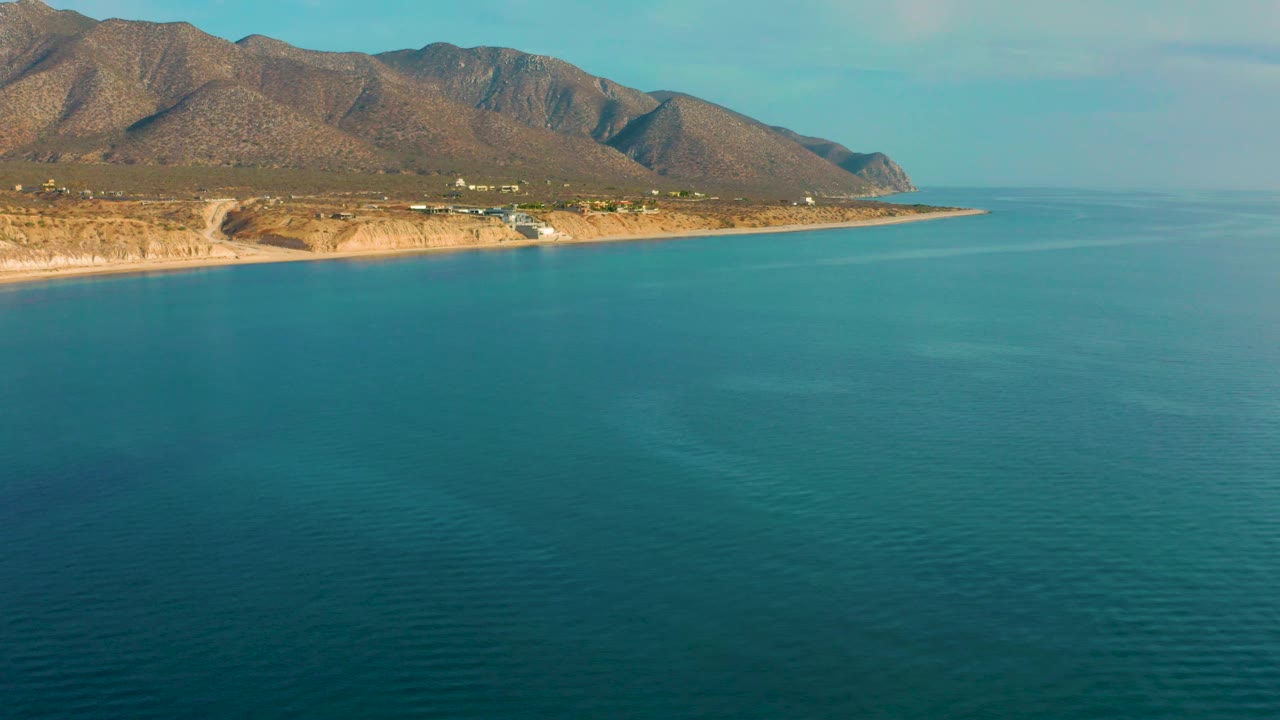 Aerial coastline with turquoise water and desert mountains in warm light.