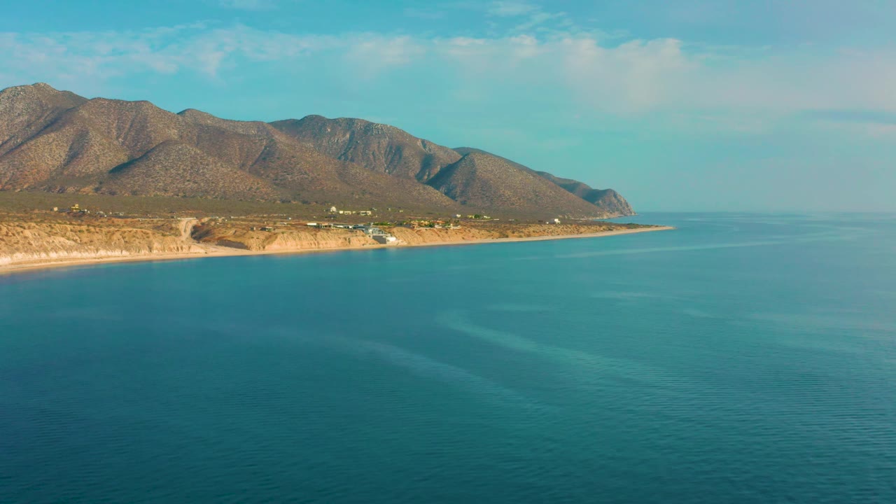 Third frame of El Sargento La Ventana, Mexico, showing the coast stretching left to right, calm turquoise sea, tan beach and bluff, dry mountain slopes, and no visible people.