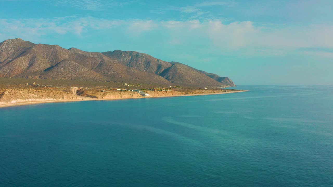 Wide opening frame over blue-green sea toward the coastline and mountain ridge of El Sargento La Ventana, Mexico, with no visible people.