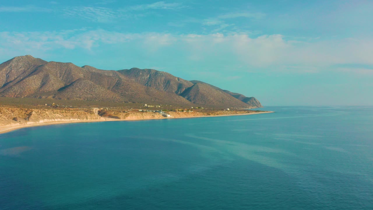 Opening frame shows El Sargento La Ventana coastline with turquoise water in the foreground, a tan shore and rugged mountains beyond, and no visible people.