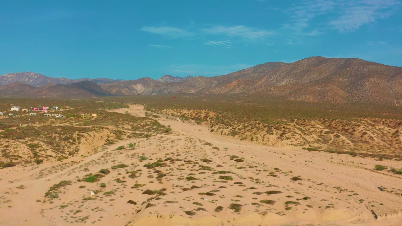Sandy desert wash crossing scrubland below rugged mountains