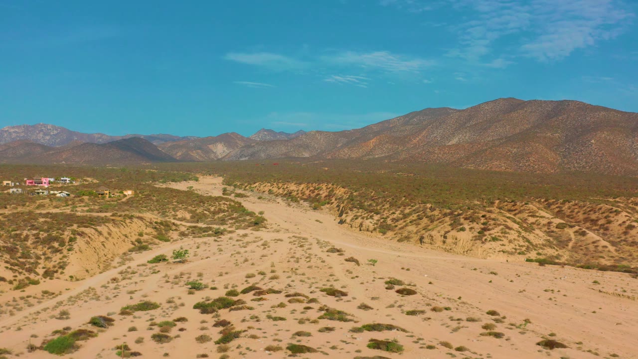 Elevated desert view with sandy wash, scrub, distant buildings, and mountains.
