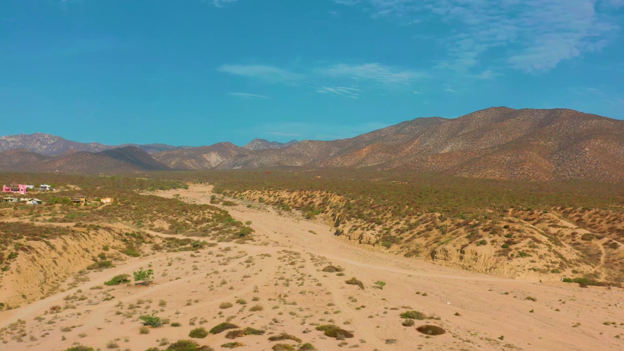 Sandy road and dry desert wash with low brush and mountains in the distance.