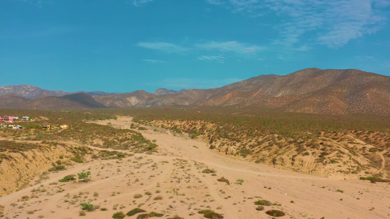 The third frame holds over El Sargento La Ventana, Mexico, with the pale road crossing the lower desert, brush patterns on the bank, a few distant buildings at left, mountains, and no visible people.