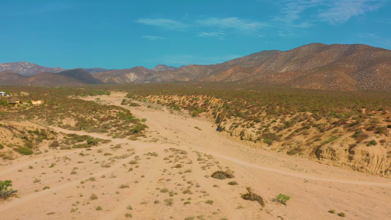 Dry desert basin with shrubs, gullies, and mountains in the distance.