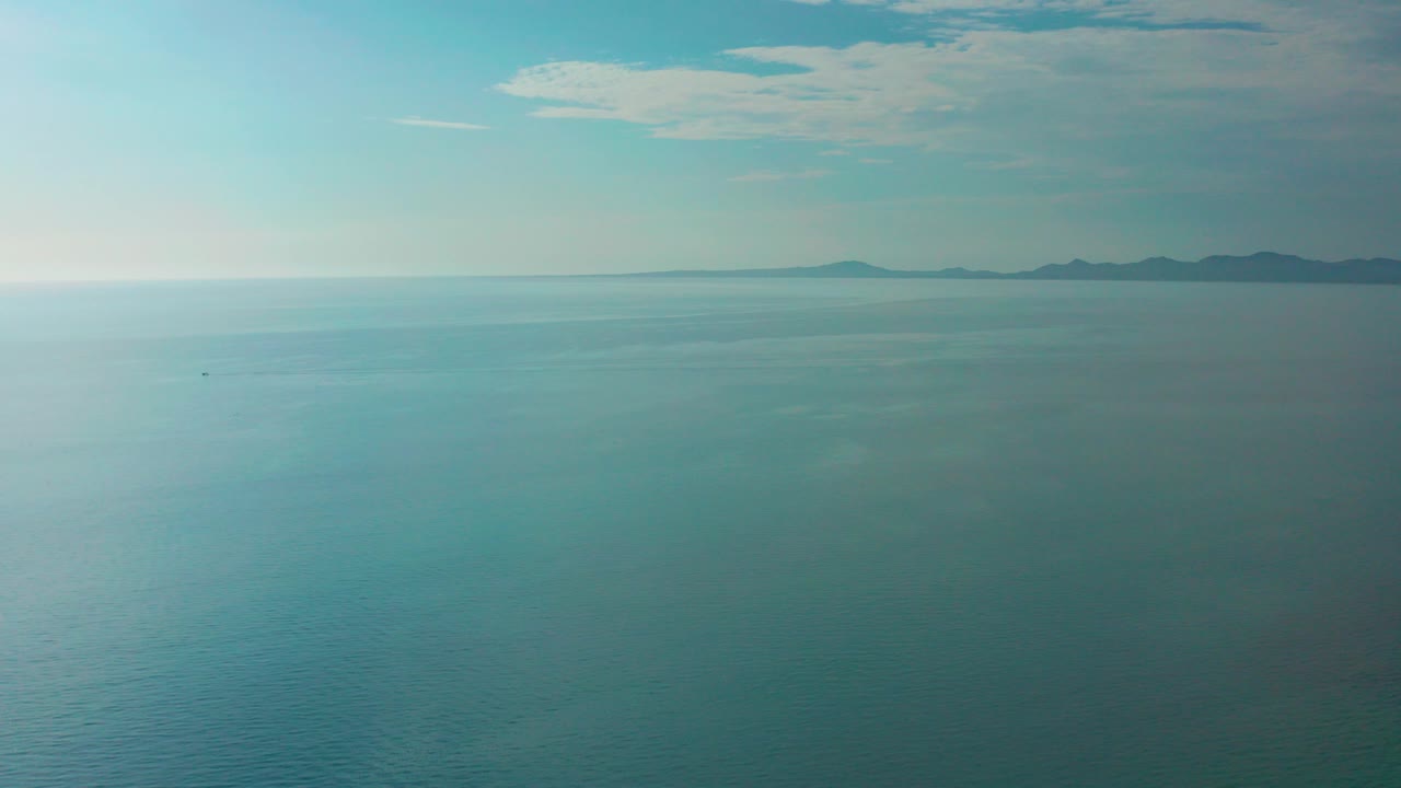 Opening frame of El Sargento La Ventana ocean footage with blue-green water, a thin horizon, distant mountainous island landforms to the right, hazy clouds, and no visible people.