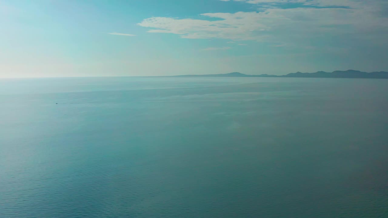 Early frame shows the El Sargento La Ventana seascape with open blue water, faint surface texture, a small dark speck far offshore, distant island ridges, and no visible people.