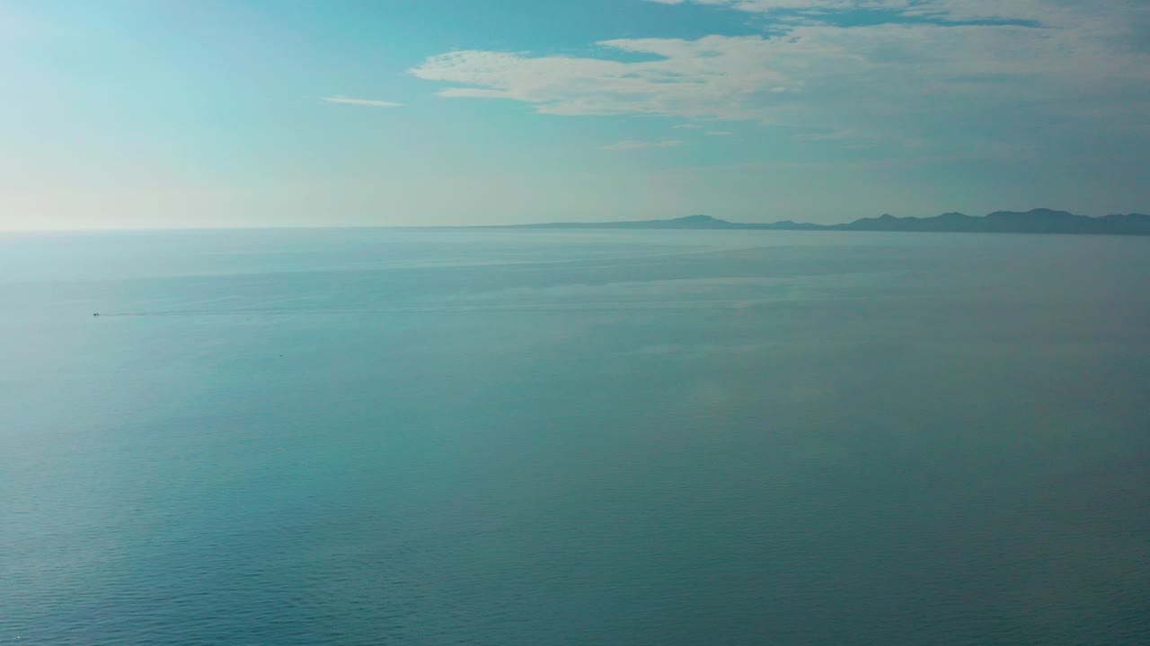 Wide ocean horizon with distant land and pale clouds
