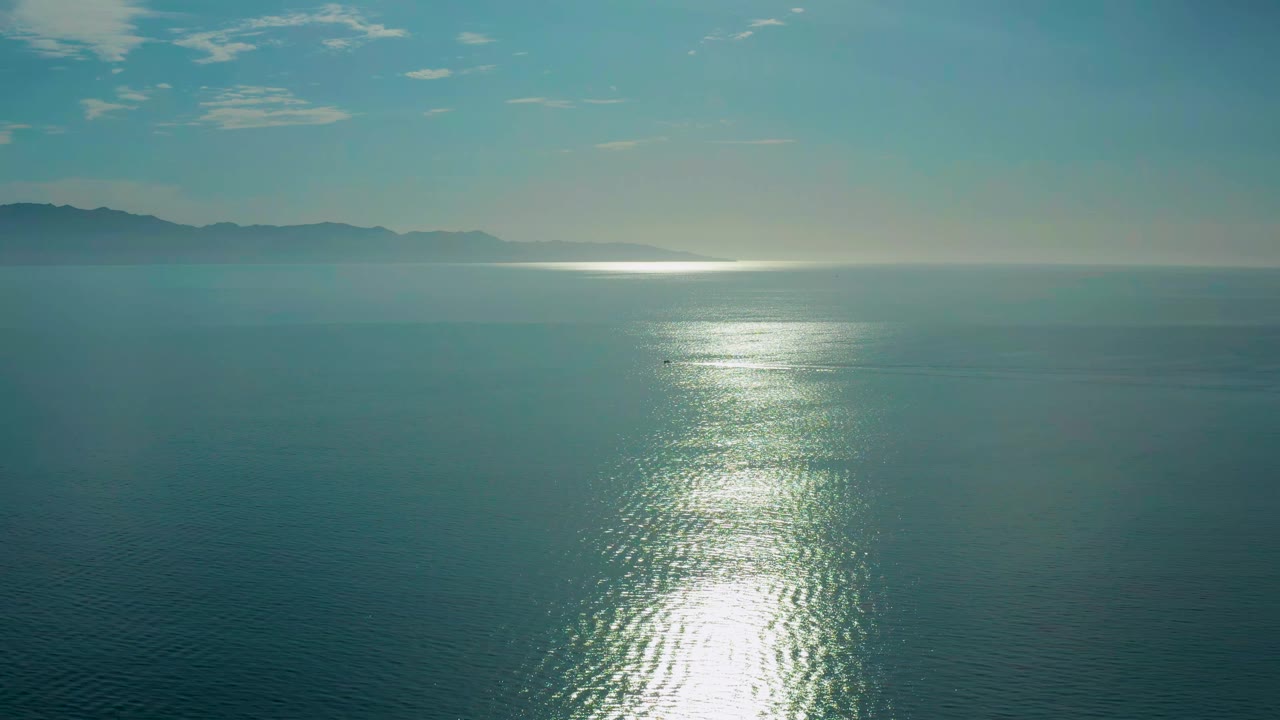 Aerial view of the ocean near El Sargento La Ventana, Mexico, with the bright reflection slightly centered on small ripples and distant land fading into haze, with no visible people.