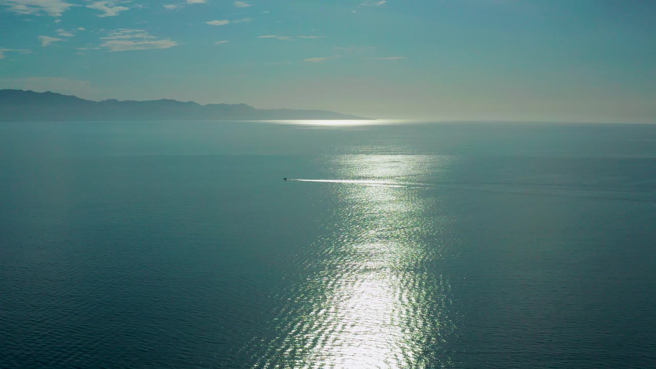 Aerial view of sunlit ocean with distant mountains on the horizon.