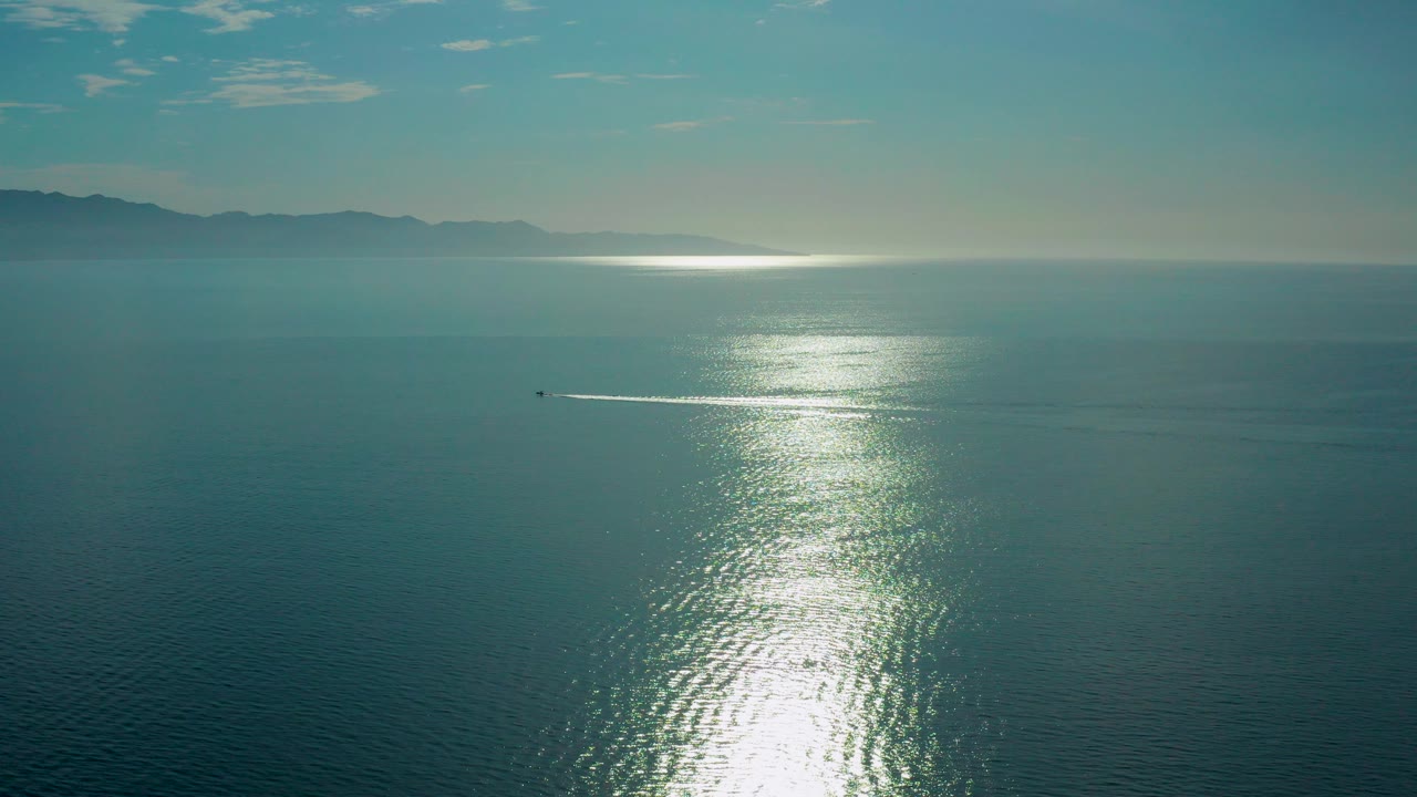 Aerial view of sun glare on calm ocean with distant mountains