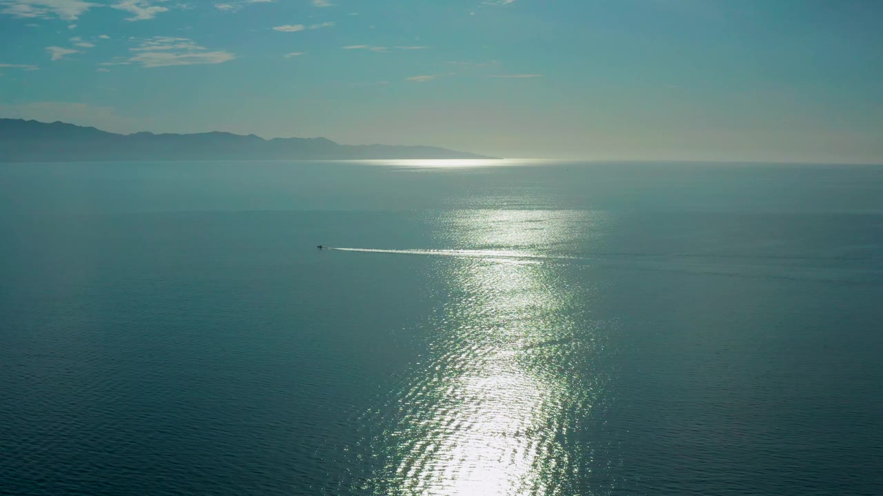 A high view of El Sargento La Ventana water shows the bright reflected sun column falling toward the foreground, a small boat wake at left center, and no visible people.