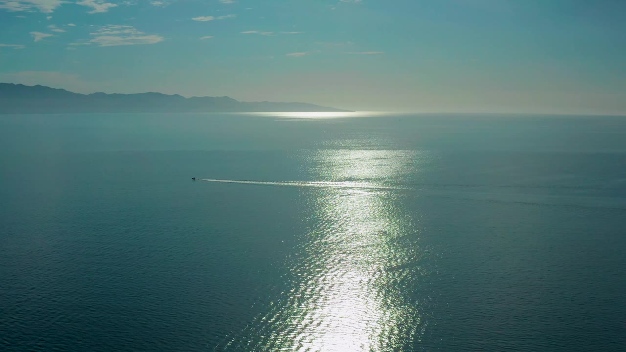 At 0:02, the boat continues across the wide ocean surface, its white wake stretching behind it while the vertical glare on the water dominates the center-right and no visible people appear.