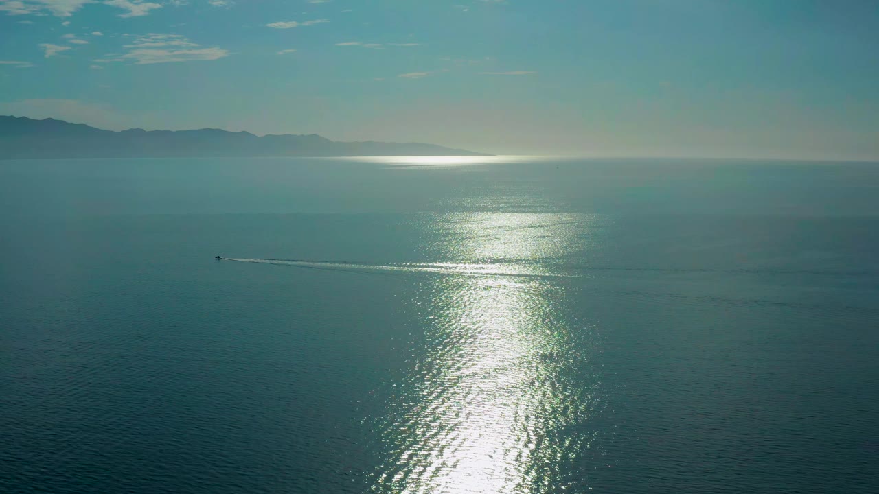 A small boat moves across the left side of the sea in El Sargento La Ventana, Mexico, leaving a thin wake below the bright vertical reflection, with no visible people.