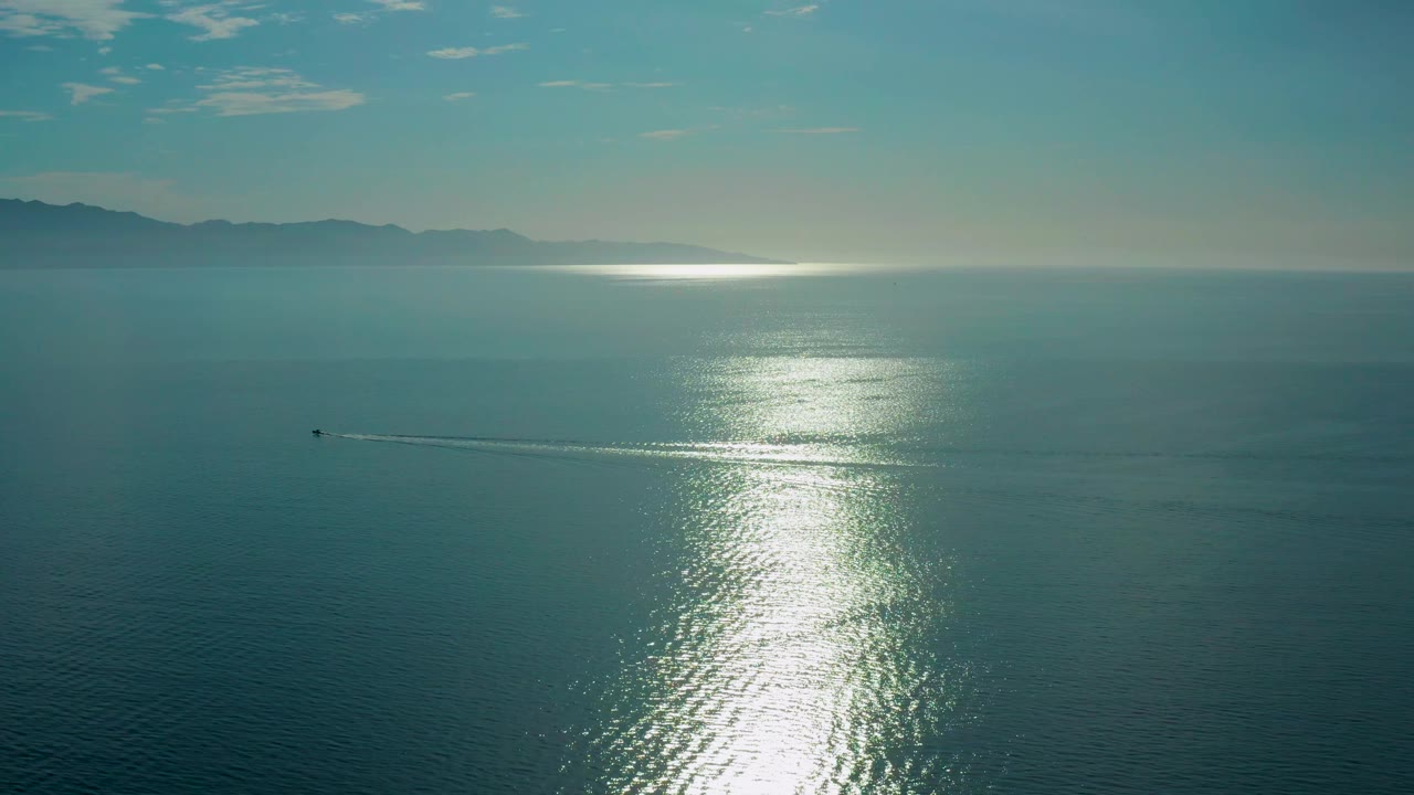 The sea in El Sargento La Ventana fills the frame as a small boat and wake cross the left midground, the sun glare brightens the lower center, and no visible people appear.