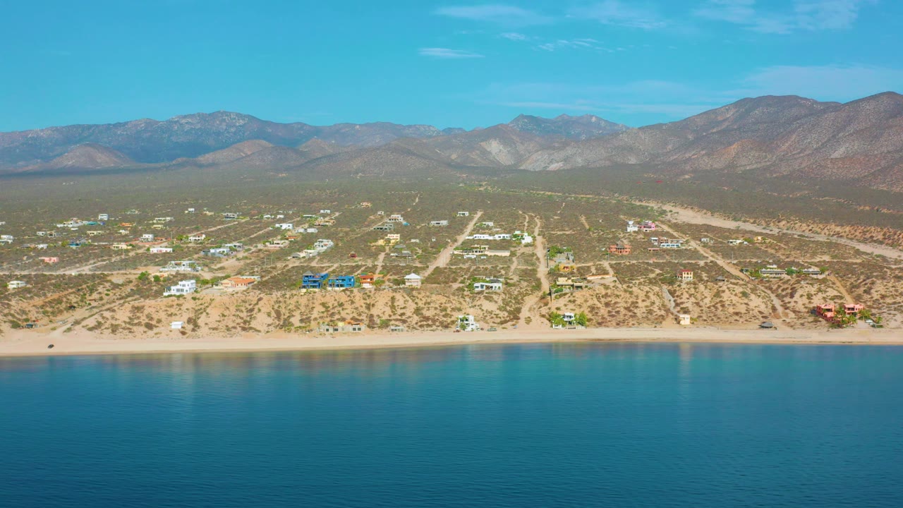 Drone view of beach and coastal neighborhood with blue water in the foreground.