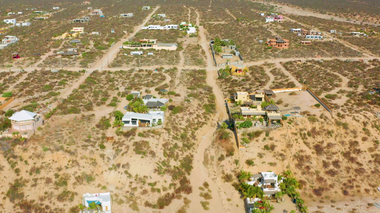 Aerial frame over El Sargento La Ventana showing sandy roads, sparse houses, scrub vegetation, distant hills, and no visible people at the opening moment.