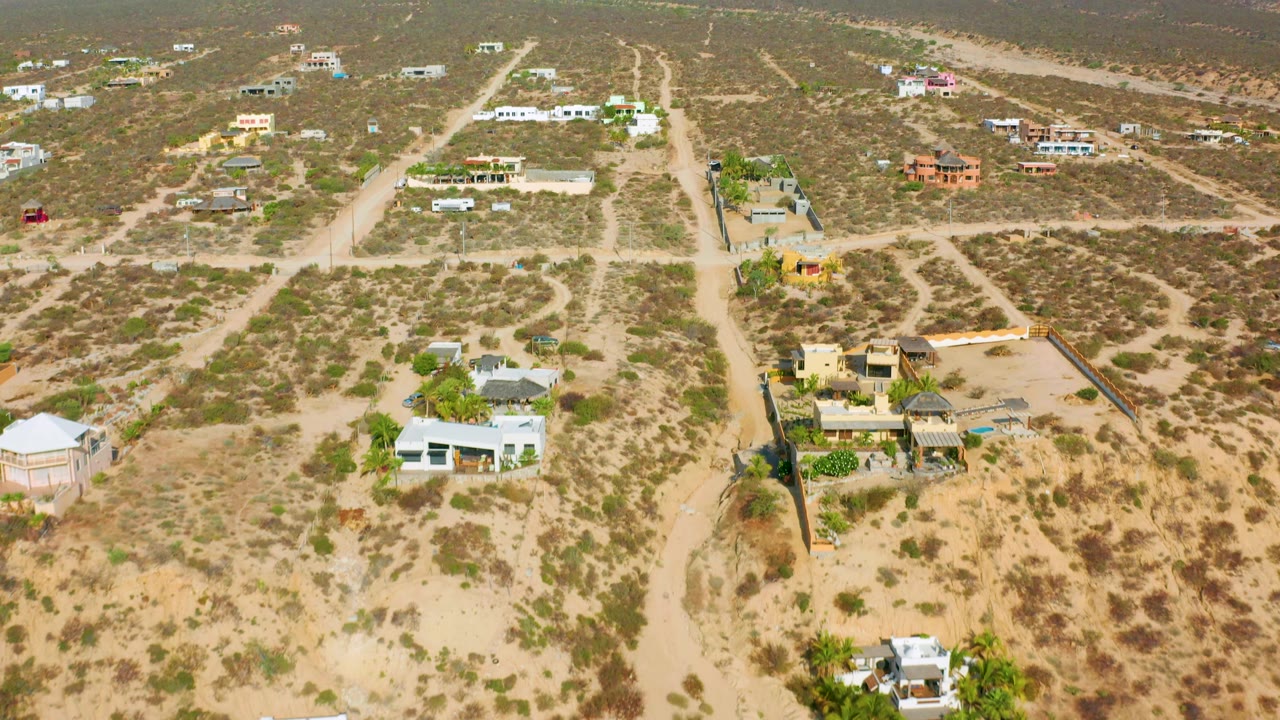 Elevated view over El Sargento La Ventana showing a pale dirt road, walled residential properties, tan desert ground, green shrubs, and no visible people.