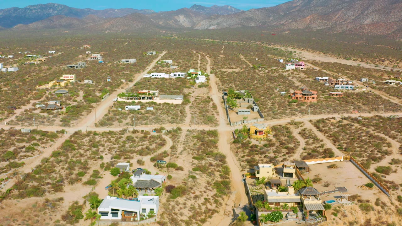 Drone-style overhead view of El Sargento La Ventana, Mexico, with a white foreground building, scattered lots, winding dirt tracks, dry terrain, and no visible people.