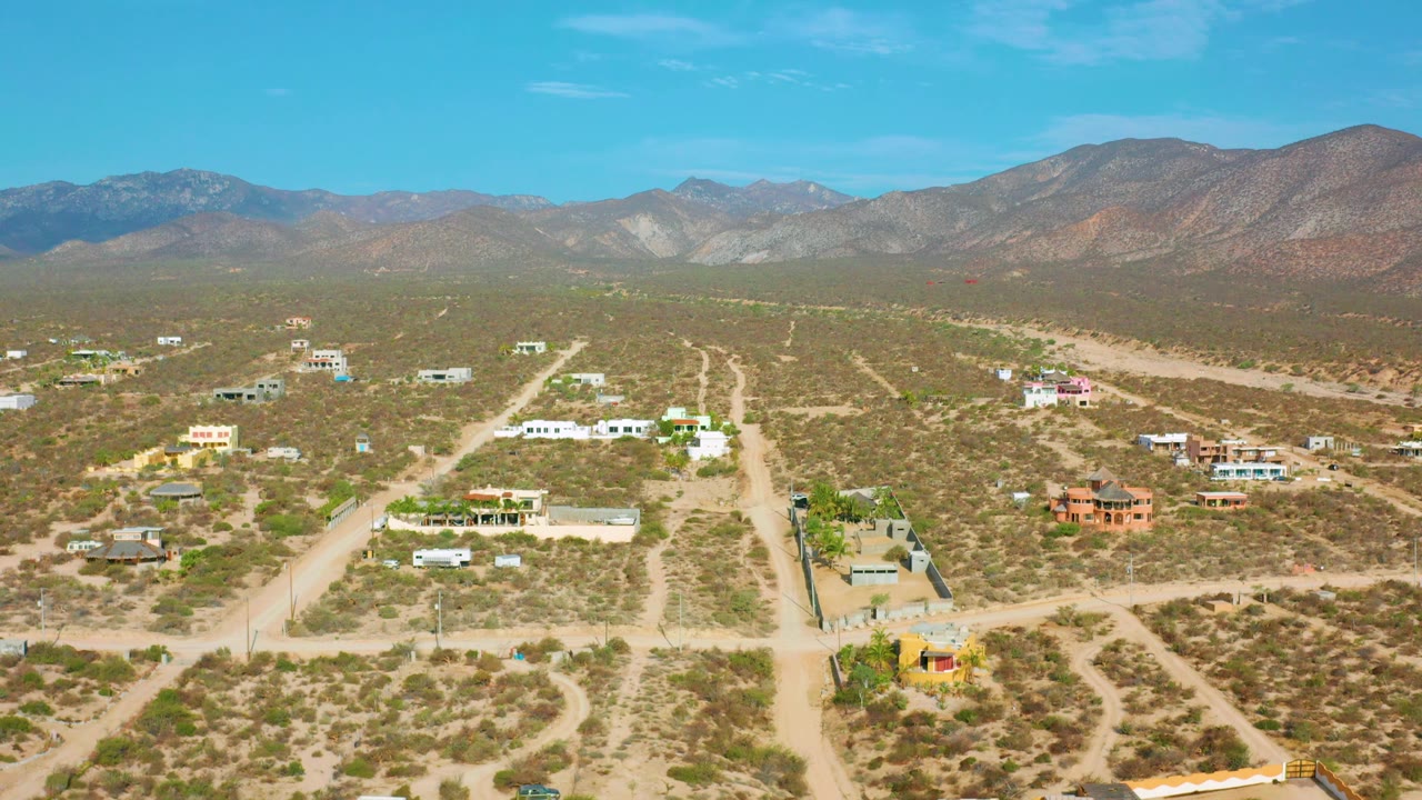 Desert village aerial with branching dirt roads and mountains in the distance.