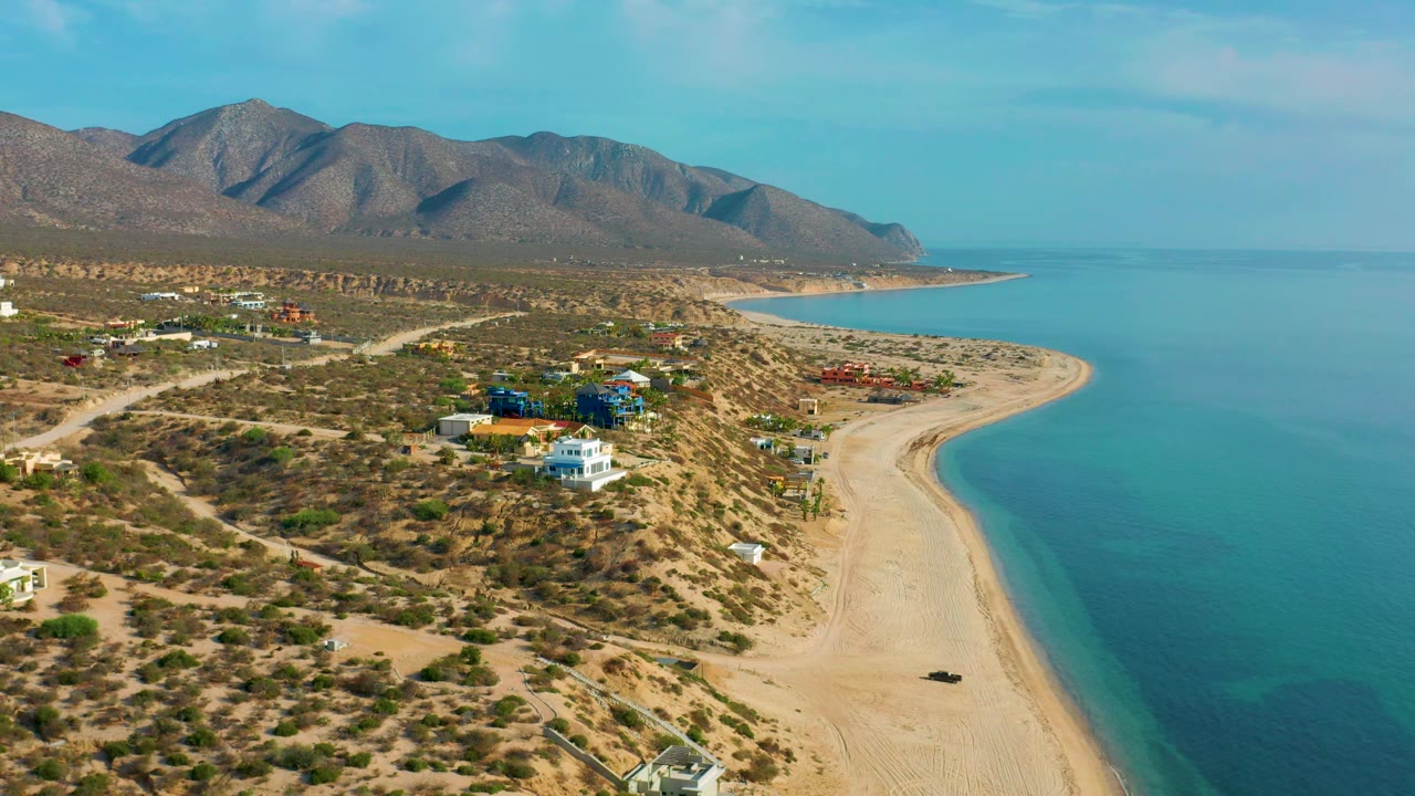 High coastal view with a white building, scrubland roads, beach, and sea.