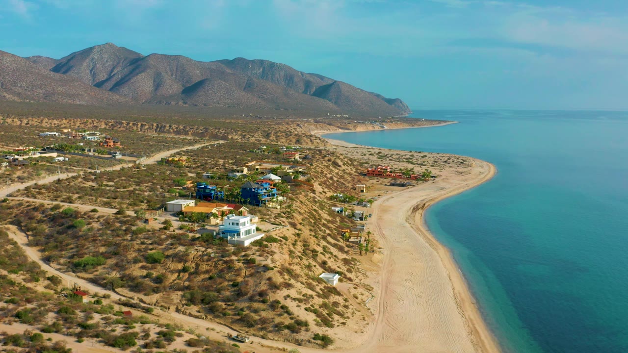 Aerial coastal landscape with hillside homes, beach, sea, and mountains.