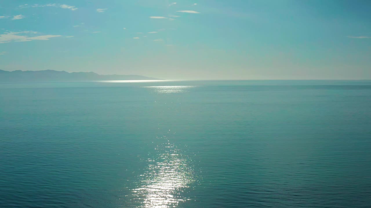 Open blue water in El Sargento La Ventana, Mexico, with the sun-glint path slightly nearer the center and faint land along the horizon, no visible people.