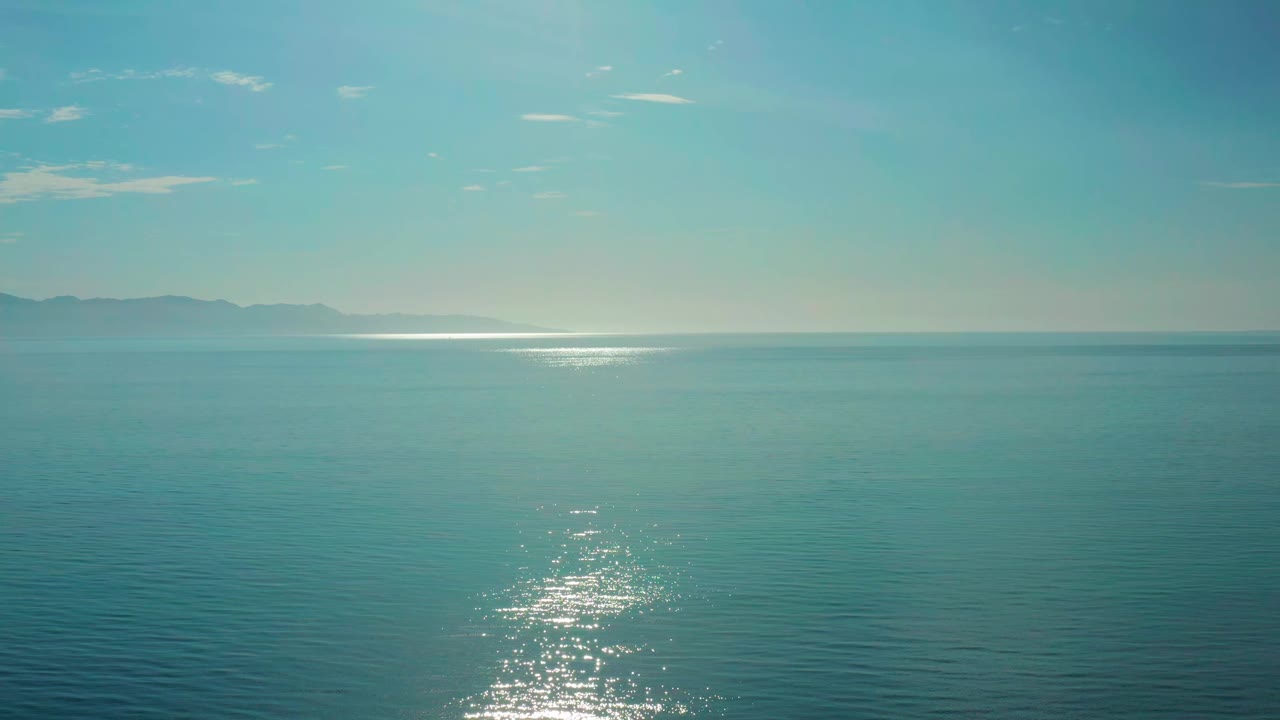 Open sea near El Sargento La Ventana, Mexico, with the sun reflection centered lower in frame, distant coastline to the left, and no visible people.