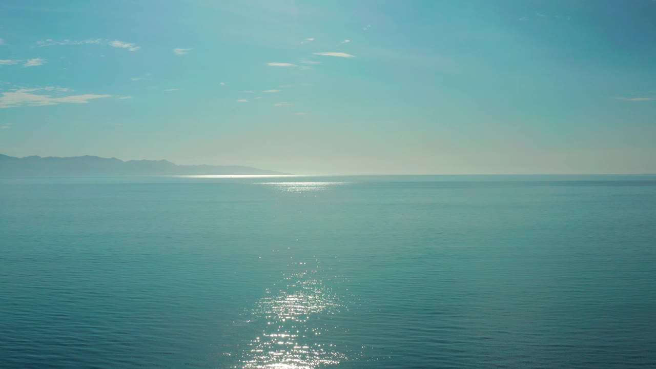 Calm ocean off El Sargento La Ventana, Mexico, with silver reflection on the blue water, faint land at left, and no visible people.