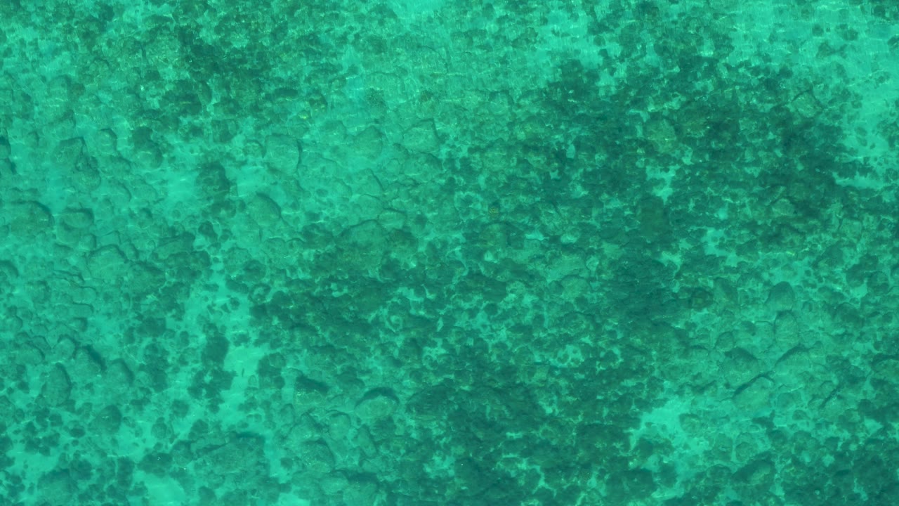 Straight-down teal water frame from El Sargento La Ventana, Mexico, with uneven dark patches beneath the surface and no boats, shore, or visible people.
