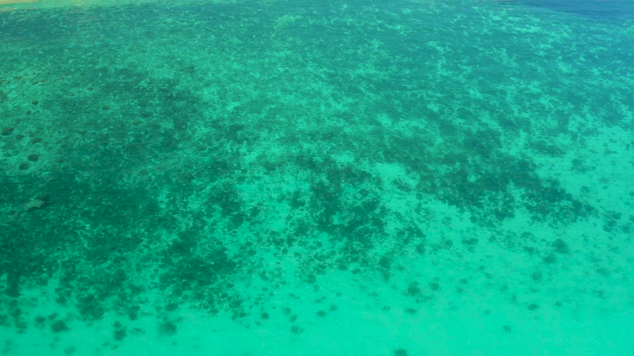 Aerial view of turquoise water in El Sargento La Ventana, Mexico, with dark submerged patches spreading across the upper half and no visible people.