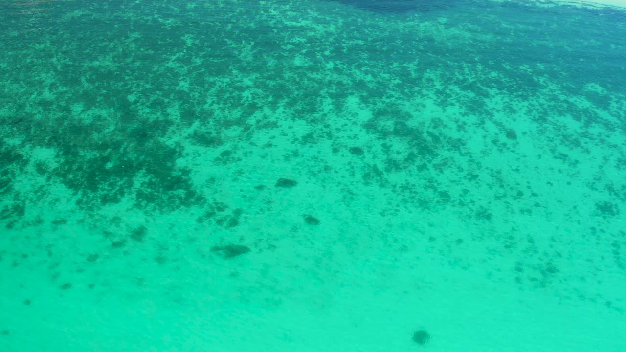 Blue-green shallow ocean in El Sargento La Ventana, Mexico, fills the frame with mottled dark seabed texture and no visible people.