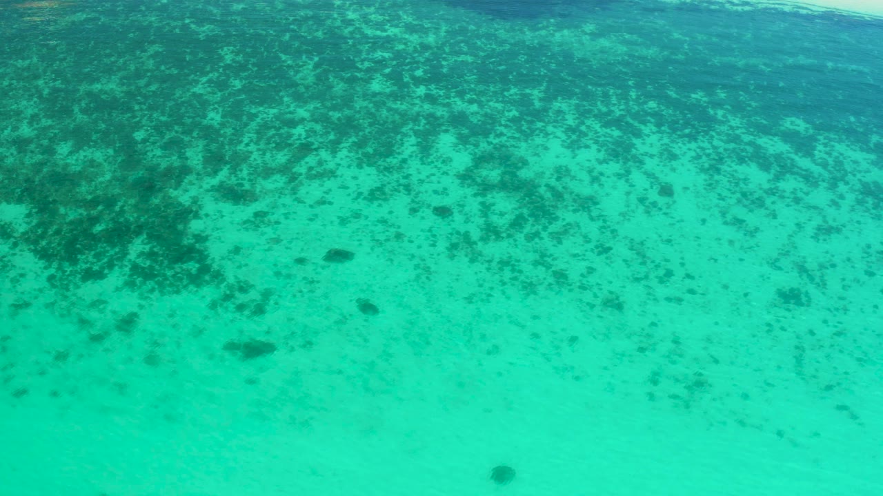 Turquoise ocean water in El Sargento La Ventana, Mexico, sits over pale sand with clustered darker seabed patches in the upper frame and no visible people.