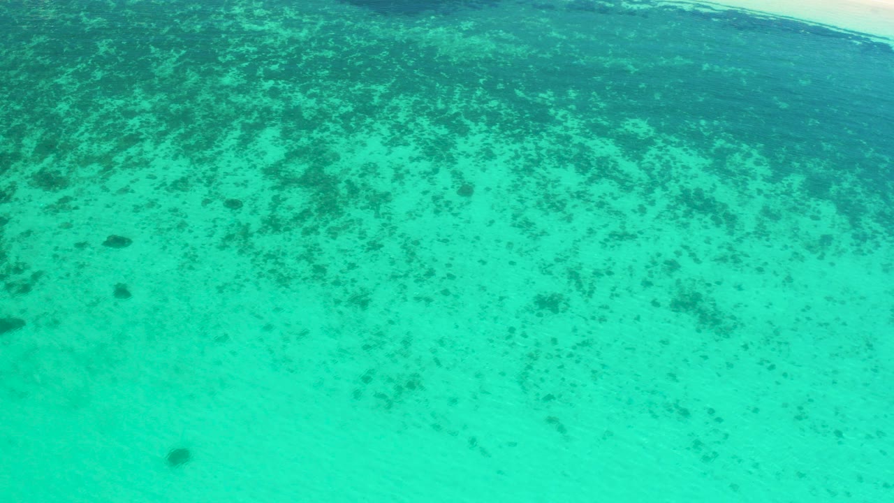High view of turquoise shallow water in El Sargento La Ventana, Mexico, with darker reef or seaweed patches across the upper half and no visible people.