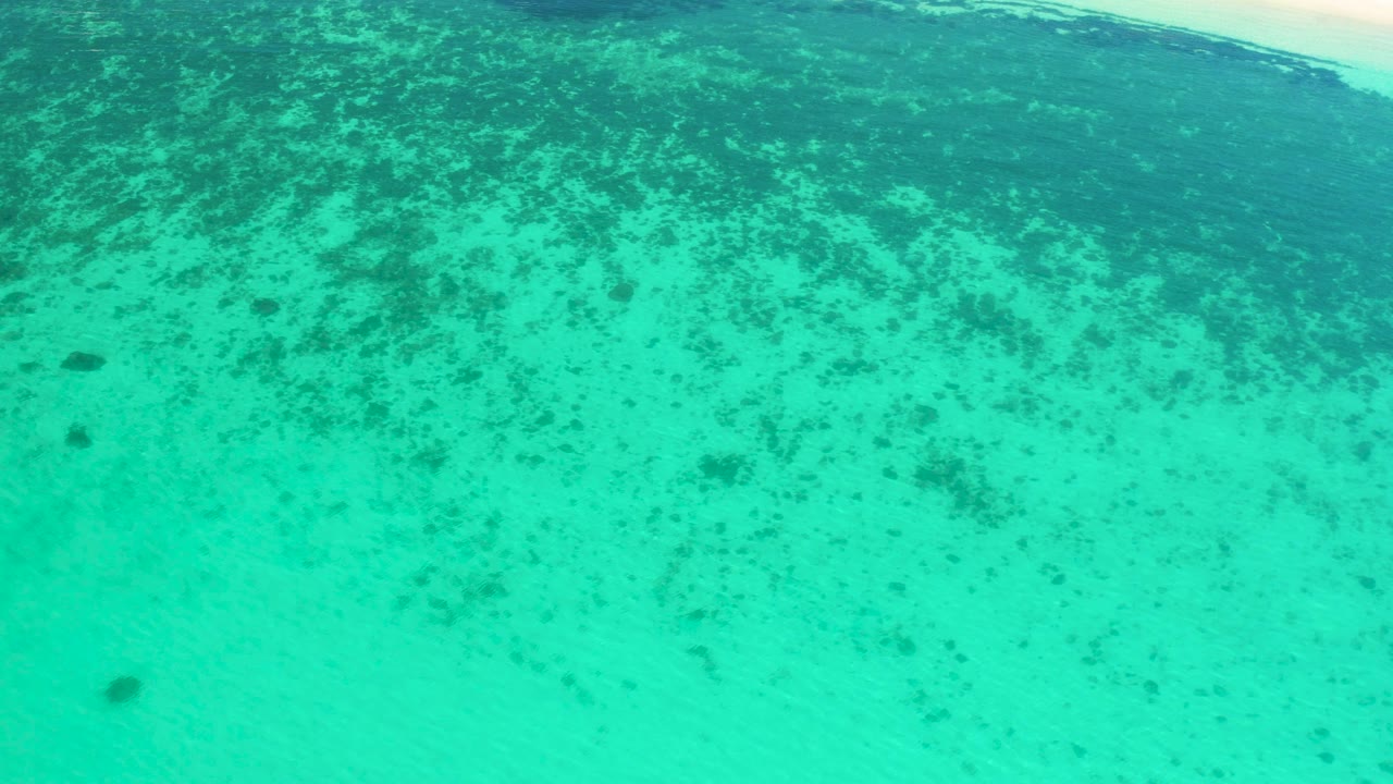 Shallow aqua water in El Sargento La Ventana, Mexico, with dark underwater patches drifting across the view and a pale surf strip near the upper edge, no visible people.