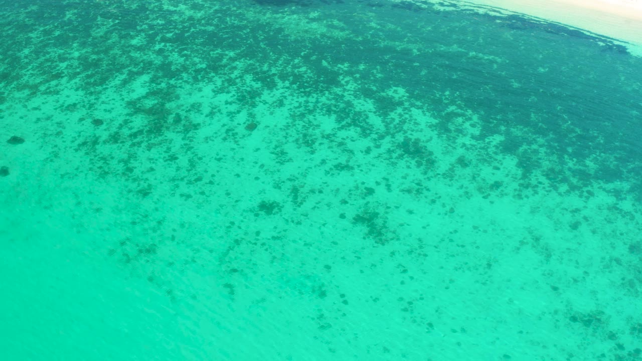 Blue-green shallows in El Sargento La Ventana show denser dark patches near the upper frame and empty water below, with no visible people.