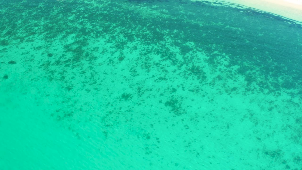 Aerial frame of turquoise coastal water in El Sargento La Ventana, Mexico, with a pale sandy strip at the top edge and no visible people.