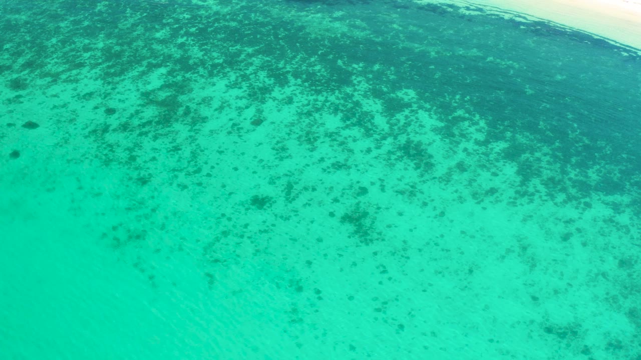 Clear shallow sea near El Sargento La Ventana appears mottled with dark underwater growth or reef-like texture, and no visible people are present.