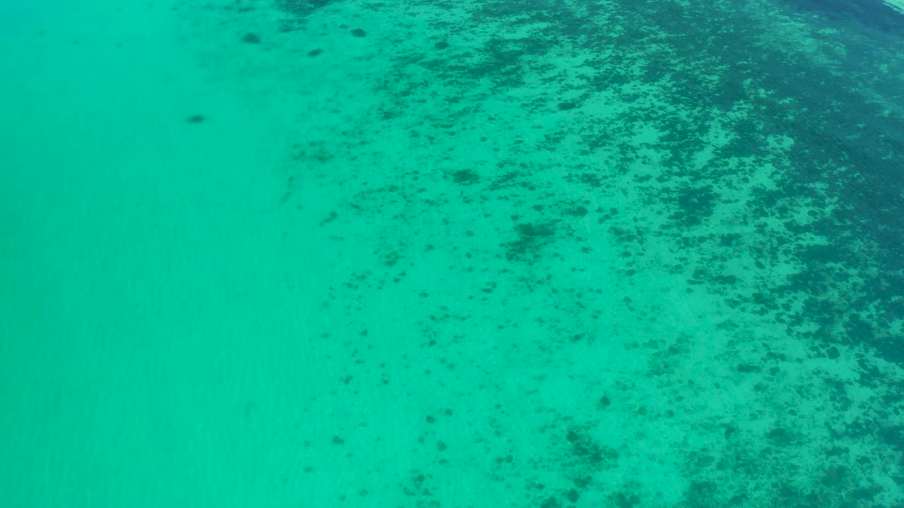 Mid-clip overhead view near El Sargento La Ventana, Mexico, showing faint ripples over turquoise water and reef texture, with no visible people.