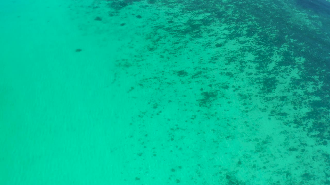 Aerial clear water with dark reef-like patches near the top.