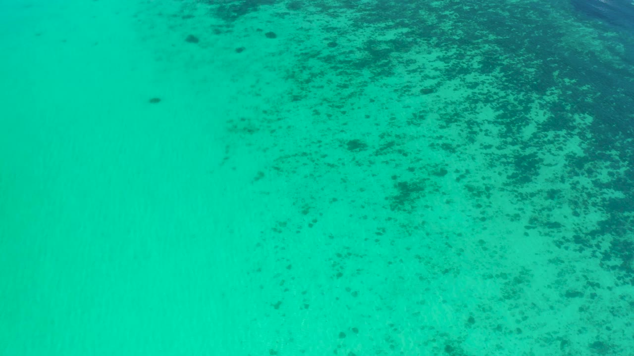 Top-down shallow ocean view in El Sargento La Ventana, Mexico, where mottled dark patches sit mostly on the right side of the turquoise water and no people are visible.