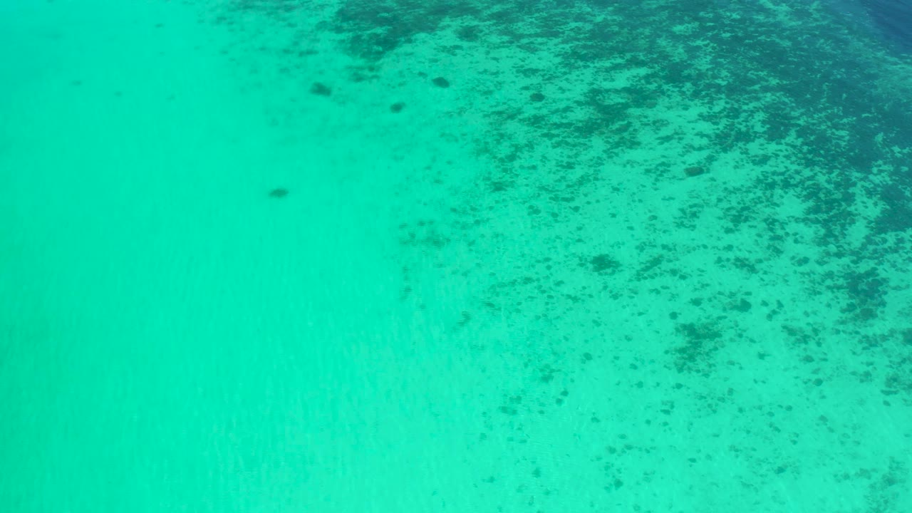 Aerial view of teal water in El Sargento La Ventana, Mexico, with mottled darker seabed visible across the right side and no visible people.