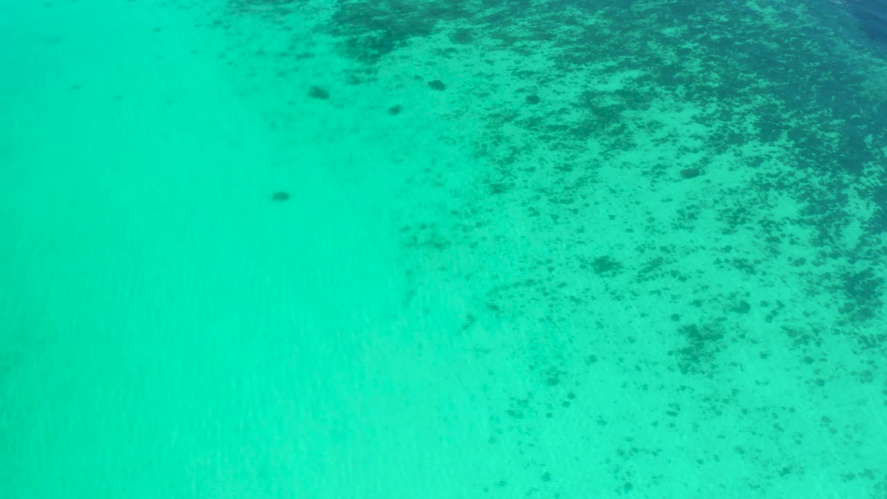 Turquoise ocean surface in El Sargento La Ventana, Mexico, with scattered dark underwater patches concentrated in the upper half and no visible people.