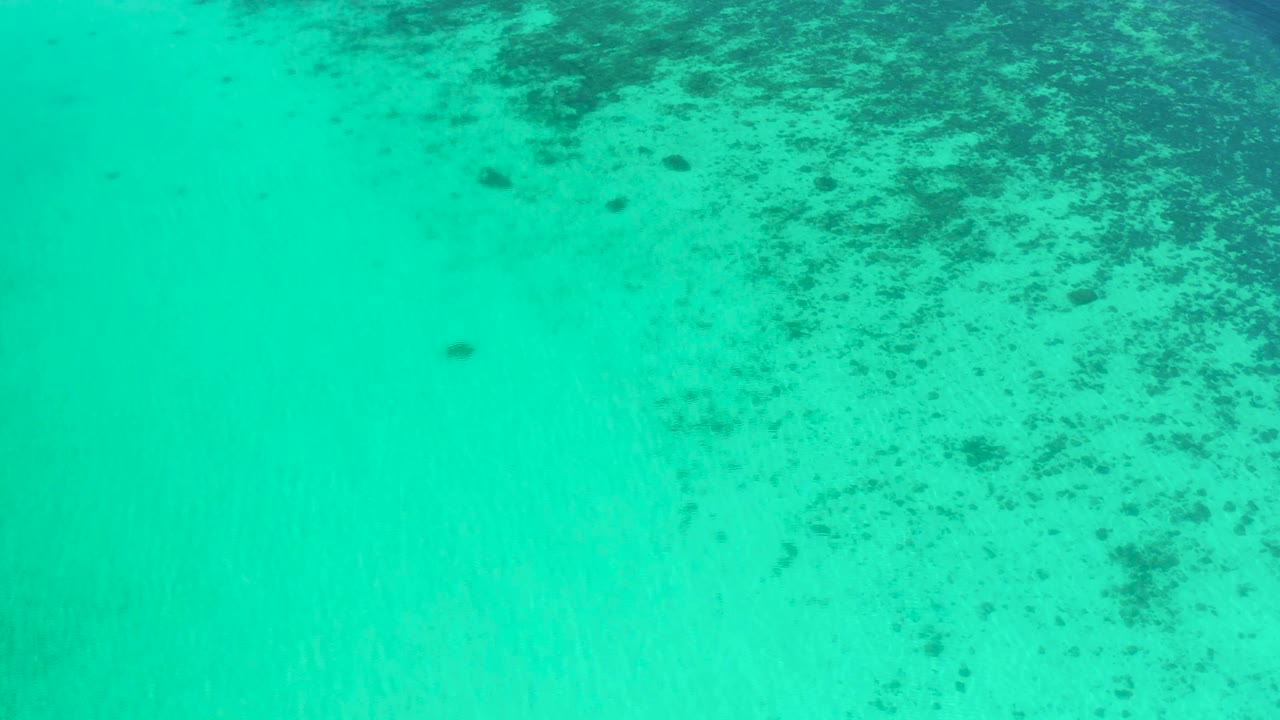 Aerial-looking view of aqua water in El Sargento La Ventana, Mexico, with pale sandy bottom visible below scattered dark underwater patches and no visible people.