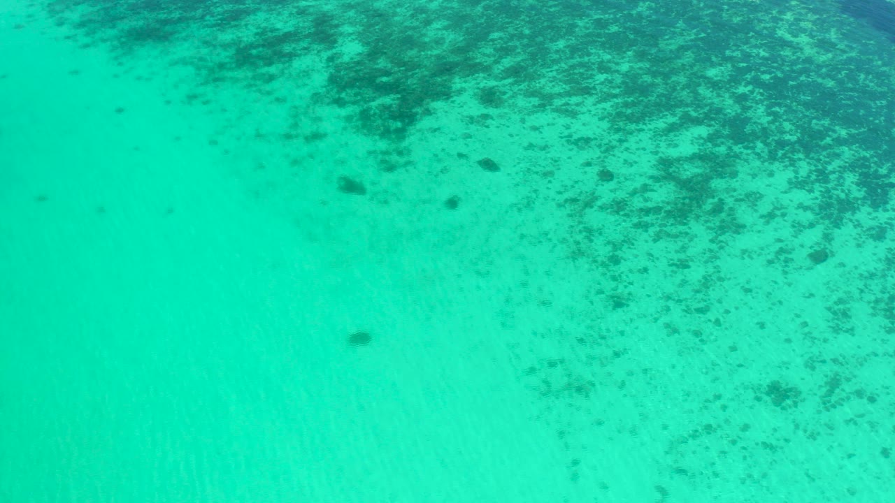 Overhead view of turquoise ocean water in El Sargento La Ventana, Mexico, with darker seabed texture concentrated near the top of frame and no visible people.
